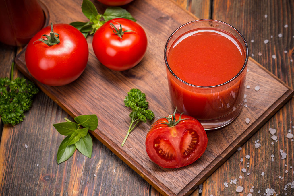 Copo de suco de tomate, tomates e folhas sobre tábua de madeira
