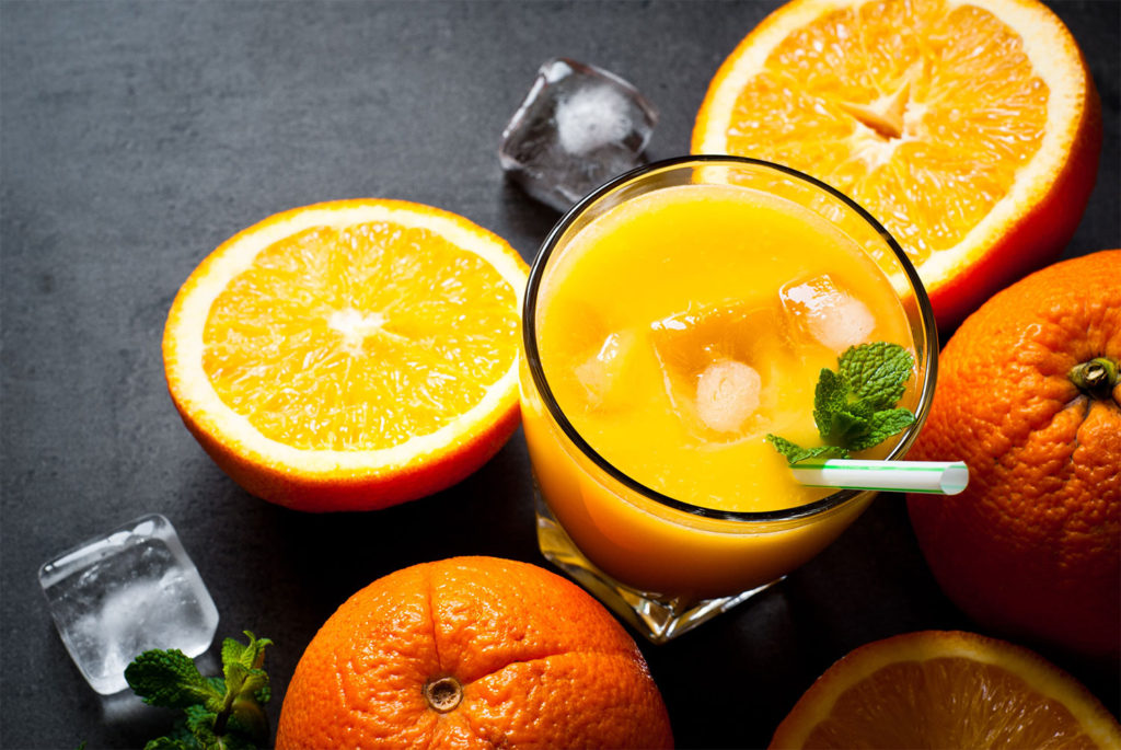 Copo de suco de laranja com folha de hortelã e laranjas ao redor