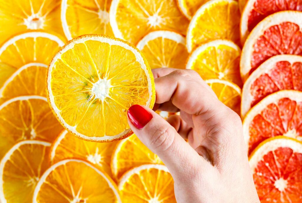mão segurando uma fatia de laranja, alimento que reforça a imunidade
